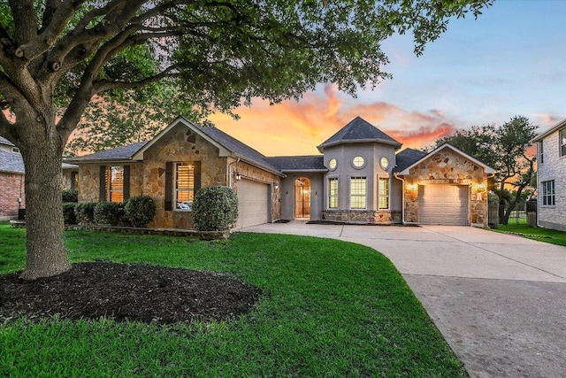 view of front facade featuring stone siding, an attached garage, concrete driveway, and a yard