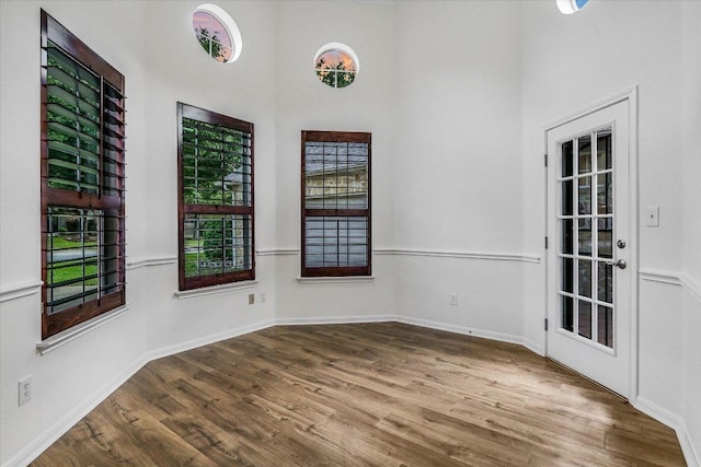empty room with wood finished floors, a high ceiling, and baseboards