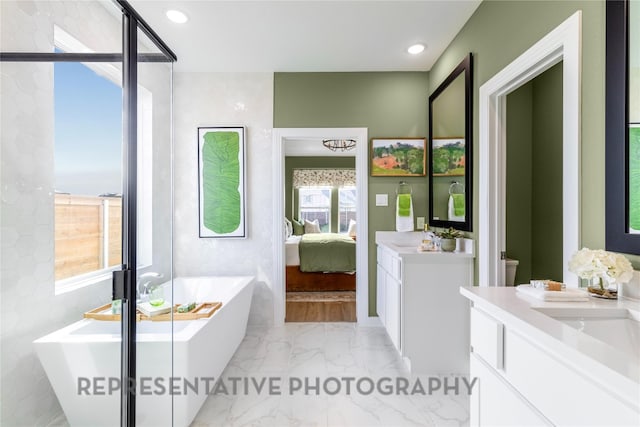 ensuite bathroom featuring vanity, marble tiled flooring, a soaking tub, and recessed lighting