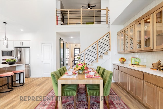 dining space featuring light wood finished floors, a ceiling fan, recessed lighting, stairway, and a high ceiling