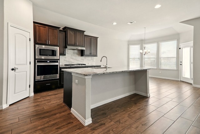 2300 La Mirada St, Leander, TX 78641 - kitchen featuring appliances with stainless steel finishes, a sink, under cabinet range hood, a chandelier, and light stone countertops
