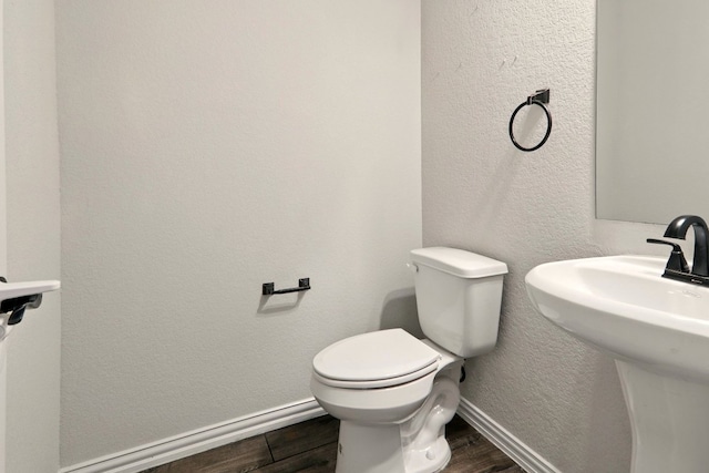 bathroom featuring wood finished floors, baseboards, toilet, a sink, and a textured wall