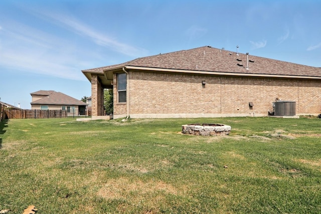 rear view of property with a fire pit, brick siding, central AC unit, and roof with shingles