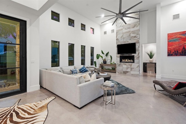 living room featuring a towering ceiling, ceiling fan, a high end fireplace, concrete floors, and baseboards