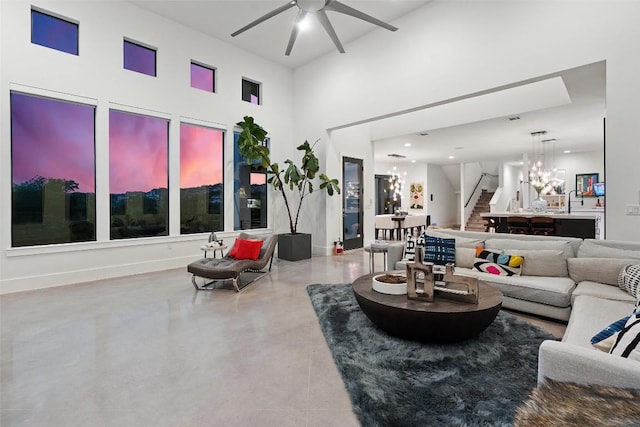 living room with ceiling fan, a towering ceiling, stairs, concrete flooring, and baseboards