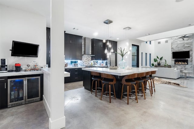 kitchen with beverage cooler, dark cabinets, wall chimney exhaust hood, and light countertops