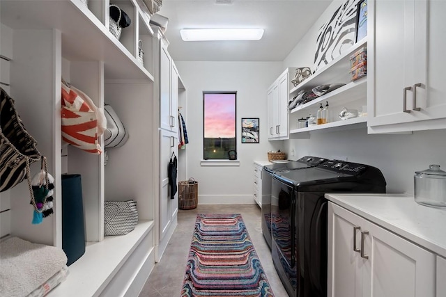 clothes washing area featuring washing machine and dryer, cabinet space, and baseboards