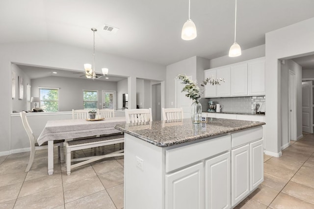 kitchen with stone countertops, light tile patterned floors, a chandelier, backsplash, and lofted ceiling