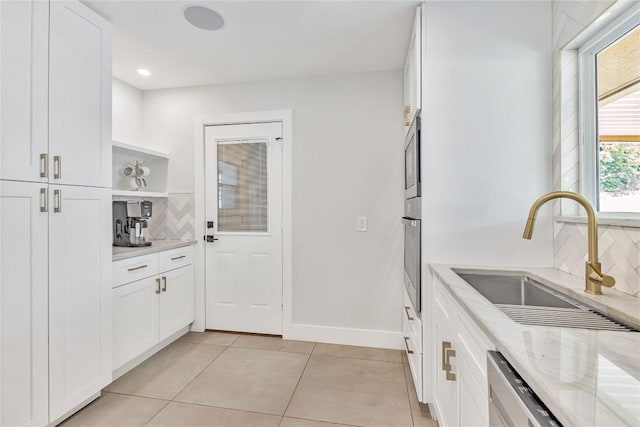 kitchen with a sink, backsplash, light tile patterned floors, white cabinets, and light stone counters