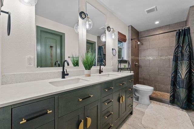bathroom featuring double vanity, a tile shower, and toilet