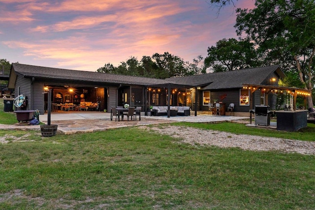 back of house at dusk with outdoor lounge area, a patio area, and a yard