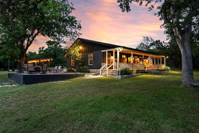 back of house at dusk featuring a yard, a chimney, and a porch