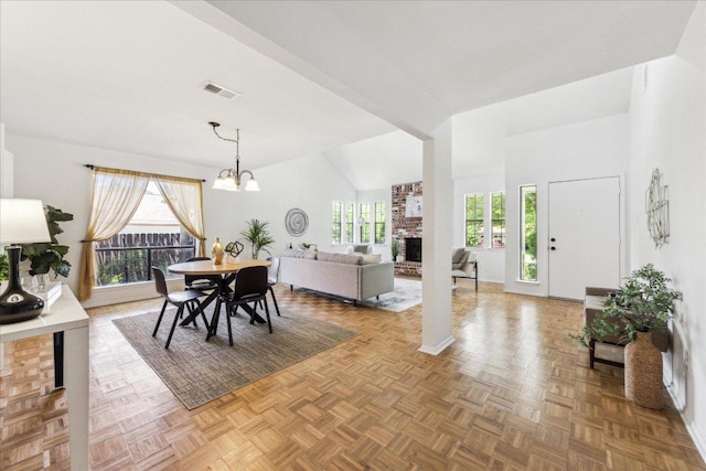 dining area featuring a brick fireplace, healthy amount of natural light, high vaulted ceiling, and a chandelier