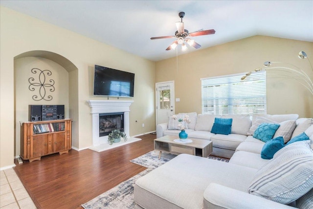 living area featuring a ceiling fan, a fireplace with raised hearth, wood finished floors, and baseboards