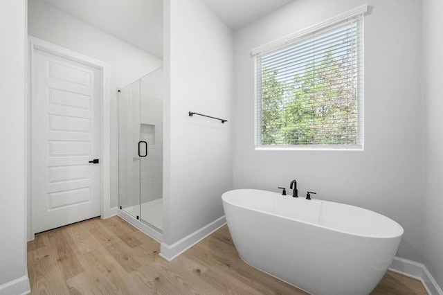 102 Kent St, Bastrop, TX 78602 - full bathroom featuring wood finished floors, a stall shower, a freestanding tub, and baseboards