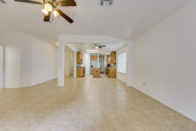 unfurnished living room featuring a ceiling fan, arched walkways, vaulted ceiling, light tile patterned floors, and baseboards