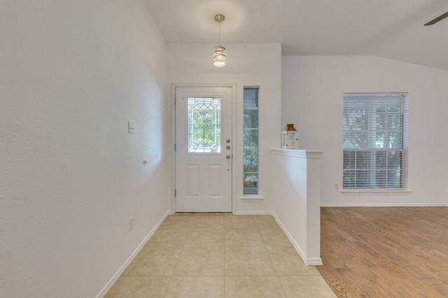 entryway with baseboards, vaulted ceiling, a ceiling fan, and light tile patterned flooring