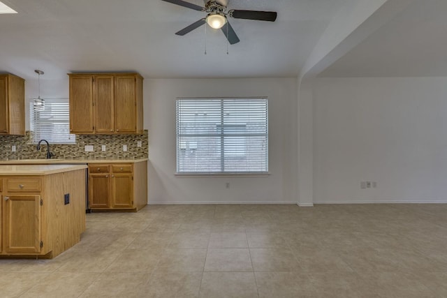 kitchen featuring light countertops, ceiling fan, decorative backsplash, brown cabinetry, and baseboards