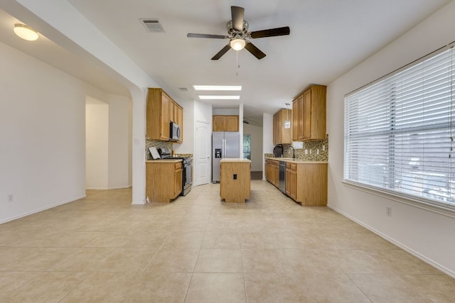 kitchen with appliances with stainless steel finishes, tasteful backsplash, a ceiling fan, and brown cabinets