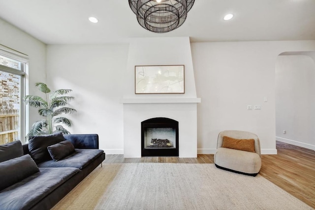 living room with wood finished floors, arched walkways, a fireplace with flush hearth, baseboards, and recessed lighting