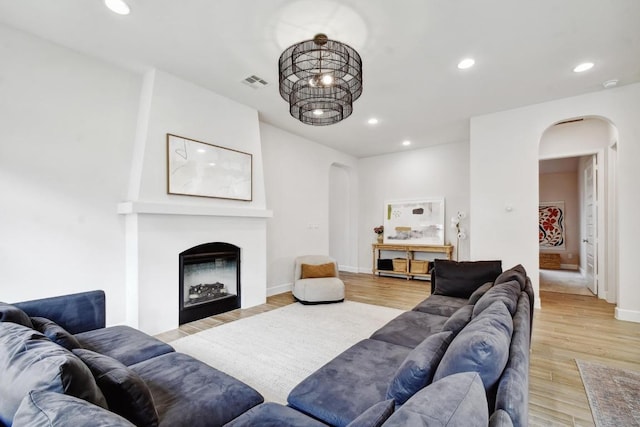 living room featuring arched walkways, recessed lighting, a fireplace, light wood-style floors, and baseboards