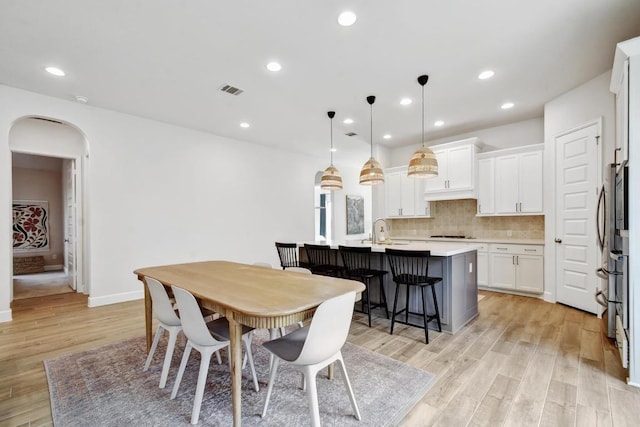 dining space featuring arched walkways, light wood-style flooring, recessed lighting, and baseboards
