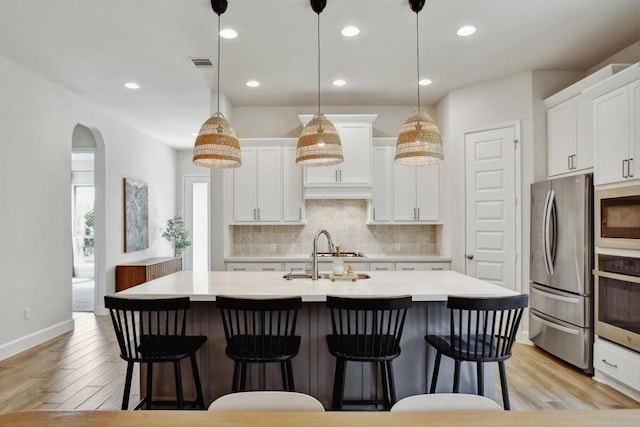 kitchen with stainless steel appliances, a sink, light countertops, light wood finished floors, and recessed lighting