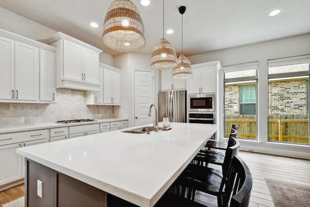 kitchen featuring stainless steel appliances, a sink, light wood finished floors, an island with sink, and decorative backsplash