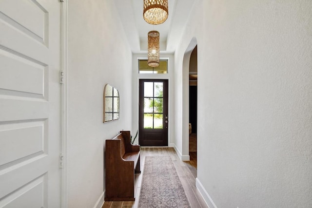 doorway to outside with arched walkways, wood finished floors, a chandelier, and baseboards