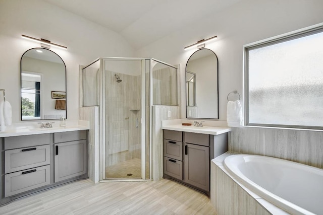 full bath featuring a stall shower, a garden tub, two vanities, and vaulted ceiling