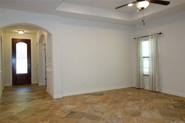 818 Caprock Canyon Trl, Georgetown, TX 78633 - empty room featuring light stone finish flooring, a ceiling fan, arched walkways, baseboards, and a tray ceiling