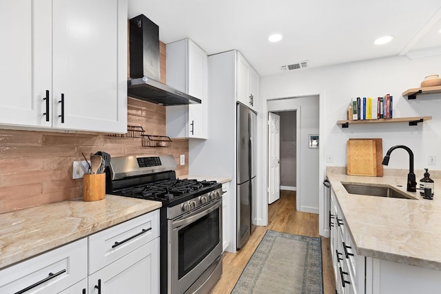 kitchen with stainless steel appliances, wall chimney exhaust hood, a sink, open shelves, and white cabinetry