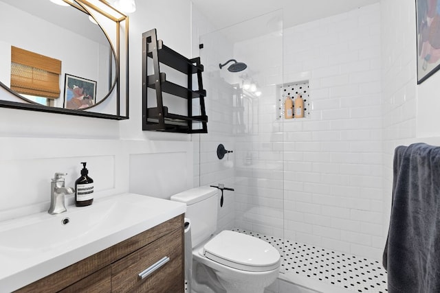 bathroom with a tile shower, toilet, vanity, and a wainscoted wall