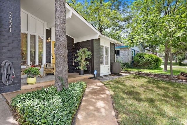 view of exterior entry featuring brick siding, a lawn, and a porch