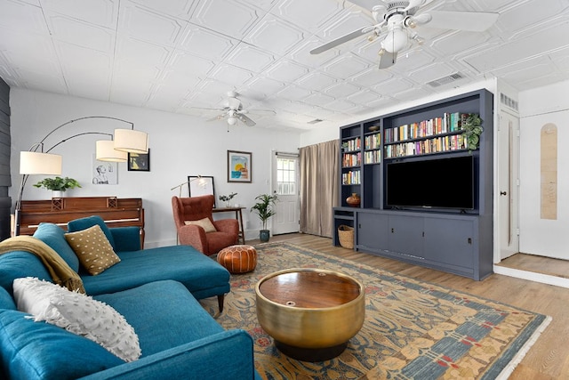 living area featuring a ceiling fan, wood finished floors, an ornate ceiling, and baseboards
