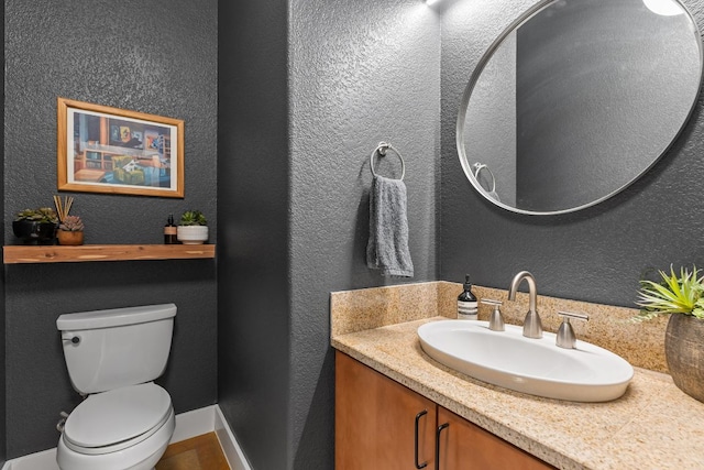half bath featuring toilet, vanity, and a textured wall