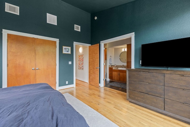 bedroom with a high ceiling, light wood-style flooring, ensuite bath, a closet, and a sink
