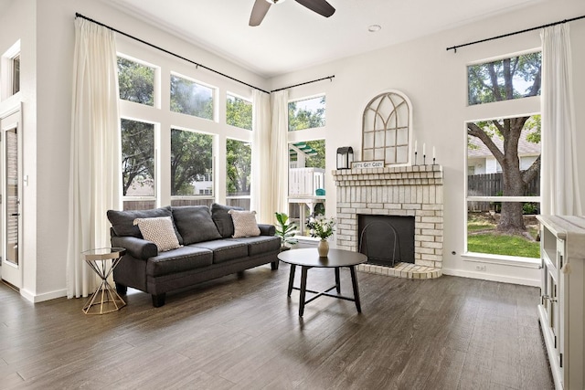living room with ceiling fan, a brick fireplace, dark wood-style floors, and baseboards
