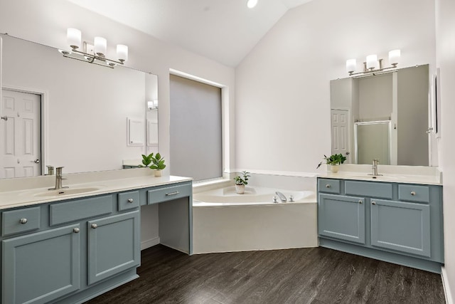 full bathroom featuring vaulted ceiling, wood finished floors, a shower stall, a bath, and two vanities