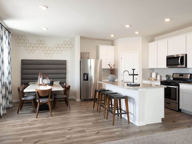 836 Sun Grove Trl, Georgetown, TX 78628 - kitchen featuring stainless steel appliances, backsplash, an island with sink, a kitchen bar, and light wood finished floors