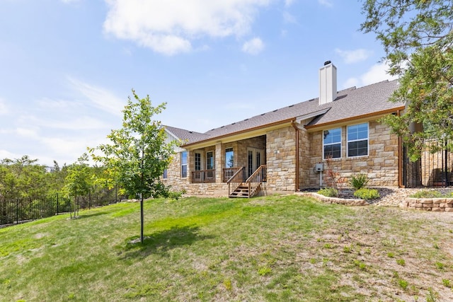 rear view of house featuring stone siding, a yard, and a chimney