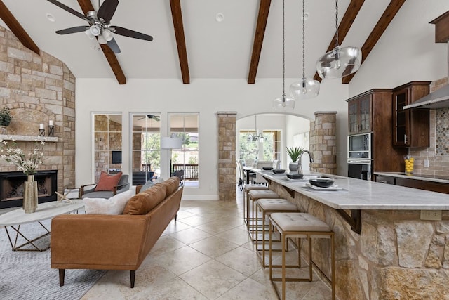 kitchen with ceiling fan, arched walkways, a kitchen breakfast bar, a sink, and high vaulted ceiling