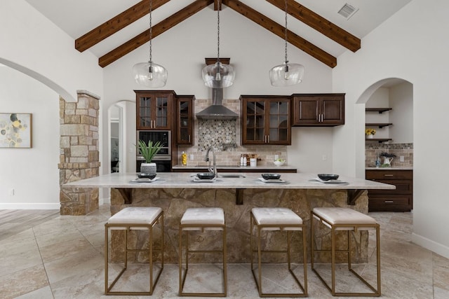 kitchen with arched walkways, stainless steel double oven, dark brown cabinetry, a breakfast bar, and backsplash