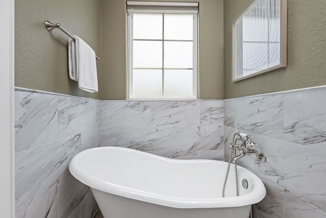 full bath with tile walls, healthy amount of natural light, a freestanding tub, wainscoting, and a textured wall