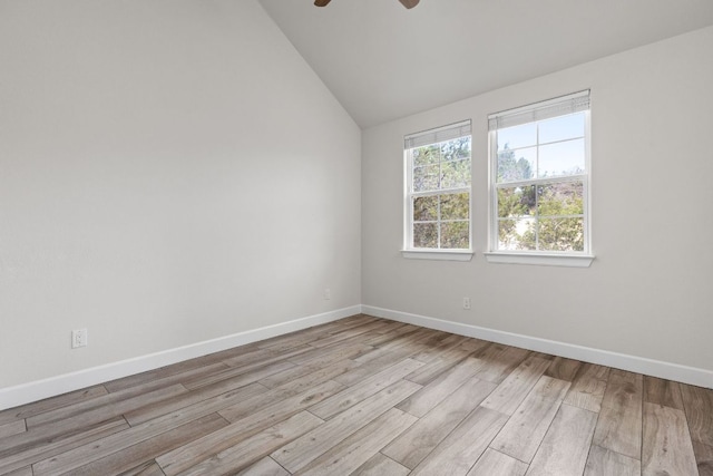 spare room featuring ceiling fan, lofted ceiling, baseboards, and light wood-style flooring
