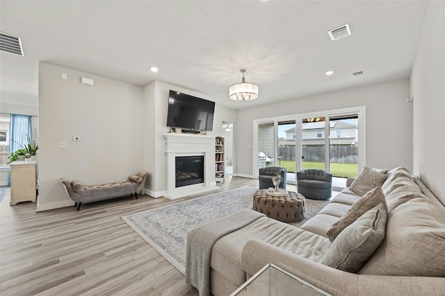living area with light wood-style flooring, a chandelier, recessed lighting, a glass covered fireplace, and baseboards