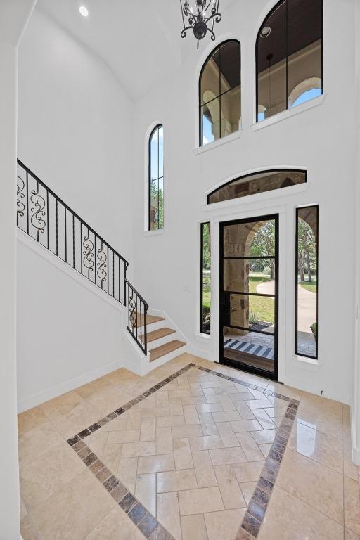 entryway featuring inlaid floor details, high vaulted ceiling, stairway, recessed lighting, and a chandelier