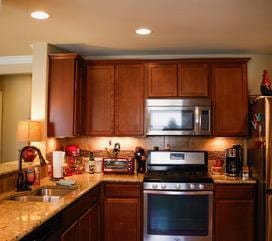 834 Salado Creek Ln, Georgetown, TX 78633 - kitchen with appliances with stainless steel finishes, a sink, recessed lighting, light stone counters, and brown cabinetry