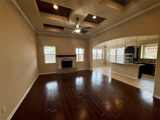 unfurnished living room featuring coffered ceiling, a brick fireplace, ceiling fan, light wood finished floors, and arched walkways