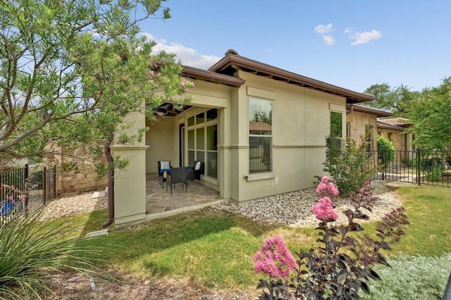 view of side of property featuring fence, a patio, and stucco siding